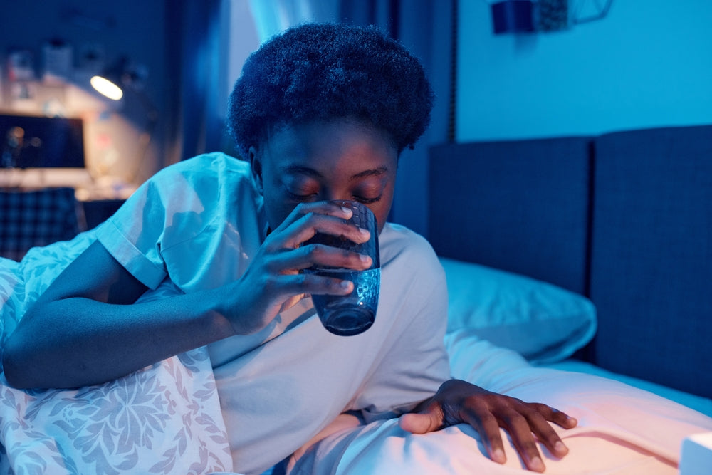 Person drinking a glass of water in bed at night, highlighting the importance of staying hydrated before sleep.